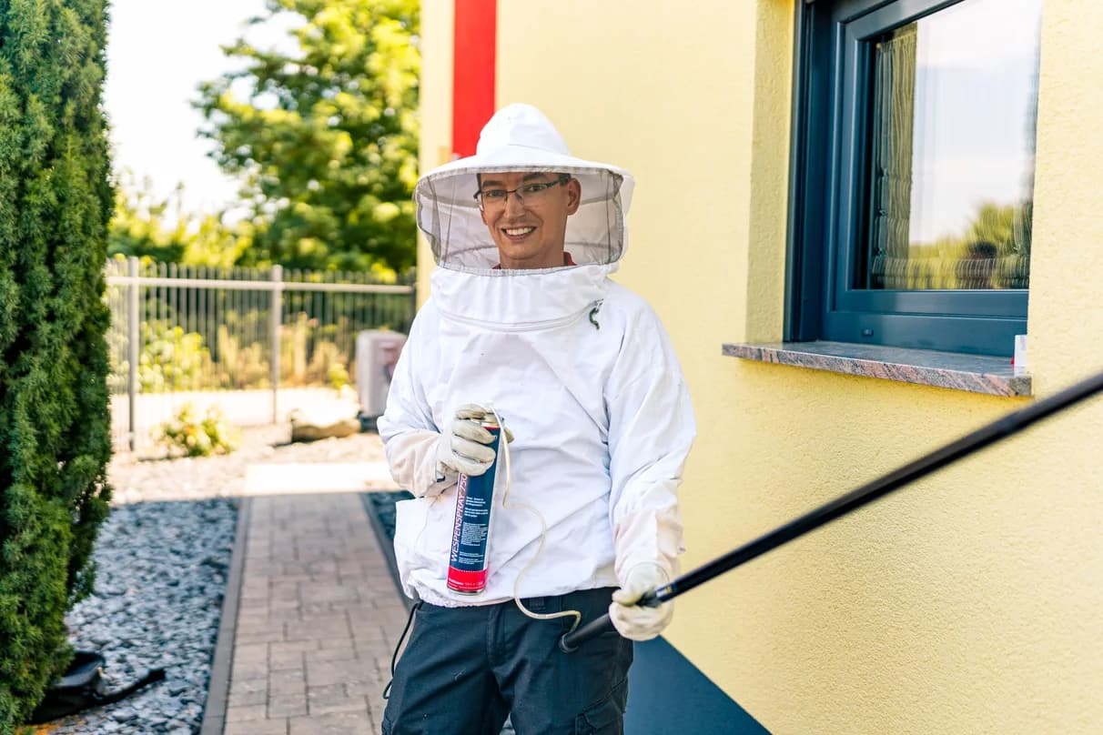 Mitarbeiter im Schutzanzug mit Sprühgerät am Gebäude